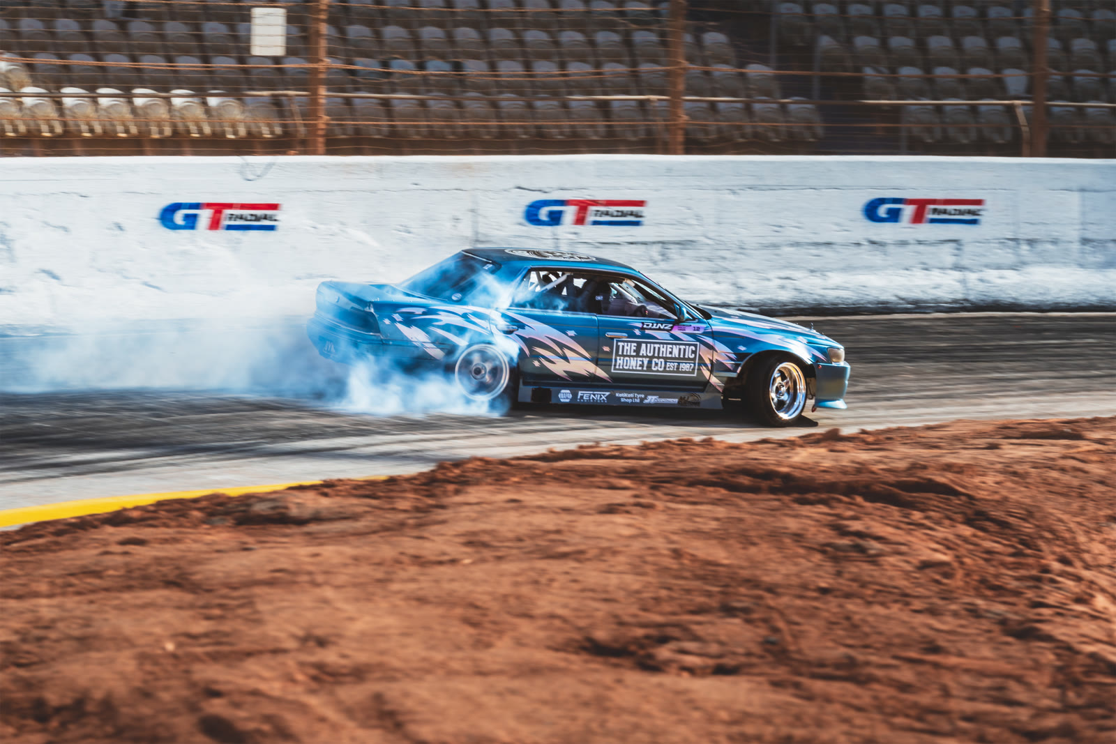 A drift car throwing smoke past the GT Radial trackside banners at D1NZ